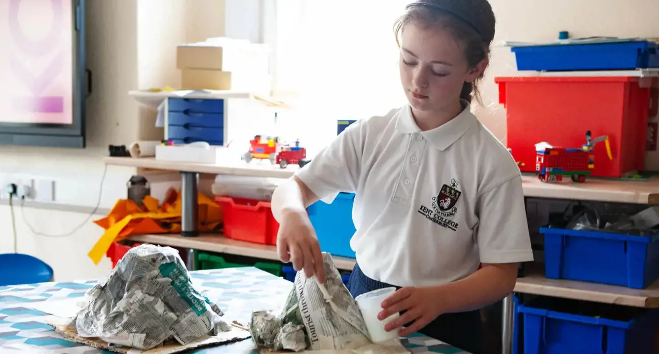 Junior school pupil at a craft club, making a papier-mache volcano